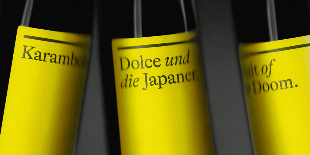 Three wine bottles with vibrant yellow labels are partially visible. Text includes "Karambolage" and "Dolce und die Japaner." The mood is stylish and contemporary.