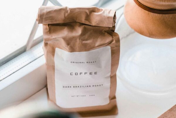 A kraft paper coffee bag with a white label sitting on a bright windowsill next to a coffee dripper.