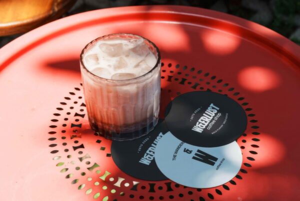 A round or square coffee coaster resting on a textured wooden or stone surface next to a warm cup of coffee.