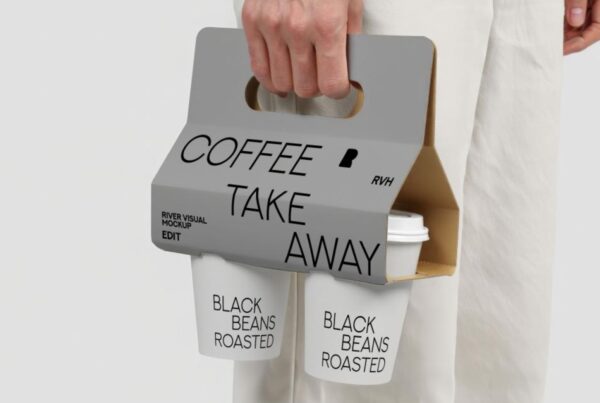 A person's hands holding a paper coffee cup and its take-away packaging in a bright, natural setting.