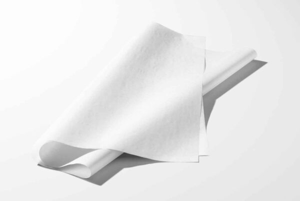 A piece of white tissue paper with soft folds and an angled perspective on a clean, light gray surface.