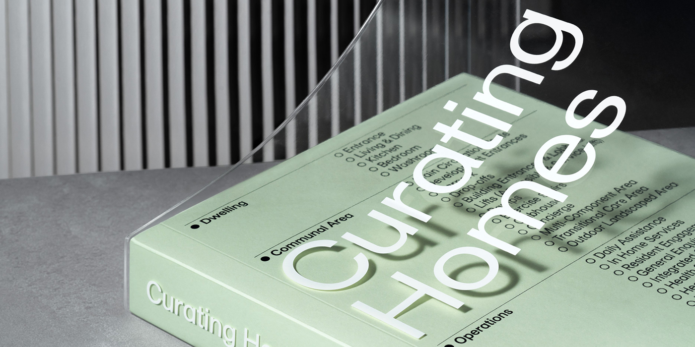 A close-up, angled shot of a pale green book titled "Curating Homes" with a transparent acrylic slipcase reflecting bold white typography.