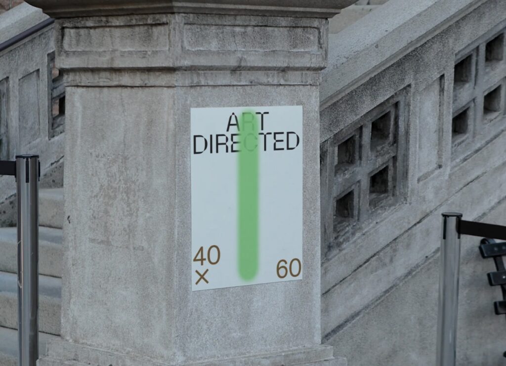 A vertical white poster with black typography and a green spray-paint detail mounted on a stone architectural pillar.