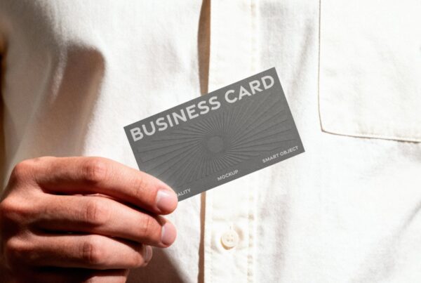 A close-up shot of a hand holding a gray business card with a sunburst pattern against a white linen shirt.