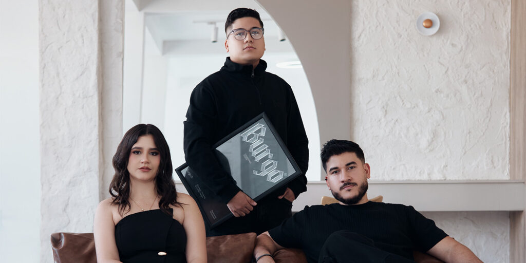 Three members of Cruzada design studio in a modern interior, with one holding a framed "Burgo" design award.