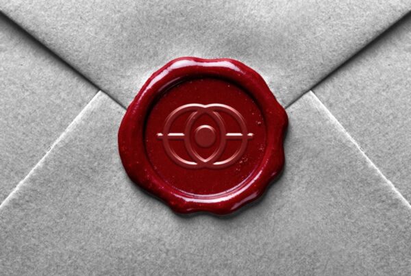 A close-up of a deep red wax seal with an embossed logo on a grey textured envelope.
