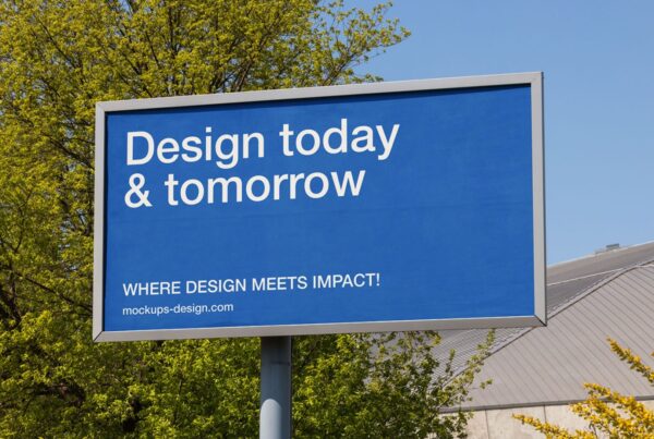 A horizontal rectangular billboard with a blue display mounted on a pole outdoors with trees and a clear blue sky.