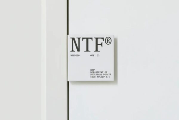 A square white wall sign with black serif typography mounted next to a vertical door frame on a white wall.