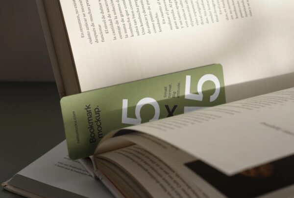 A close-up view of a green paper bookmark with bold "5x15" typography placed vertically inside an open book under sharp, direct sunlight.