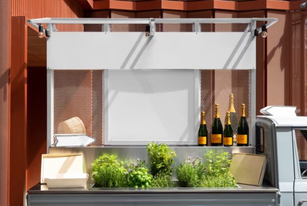 A close-up view of a modern catering truck bed customized with a blank white menu board, overhead sign, fresh herbs, and champagne bottles.