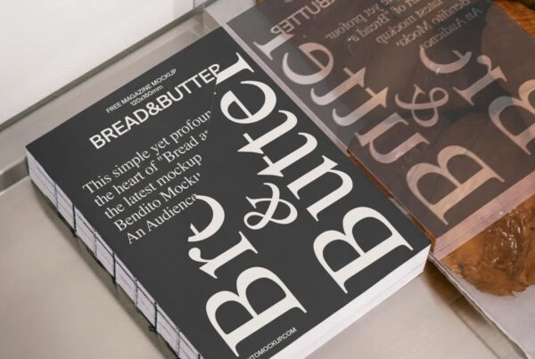A stack of black magazines titled Bread & Butter sits on a metal counter next to a glass bakery display reflecting the cover typography.