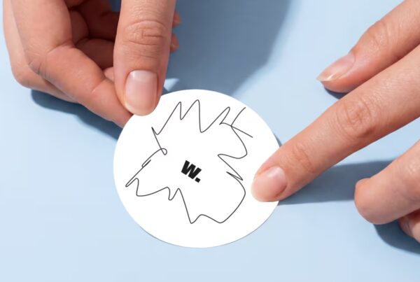 Hands carefully applying a round sticker onto a smooth, flat surface in a softly lit studio setting.