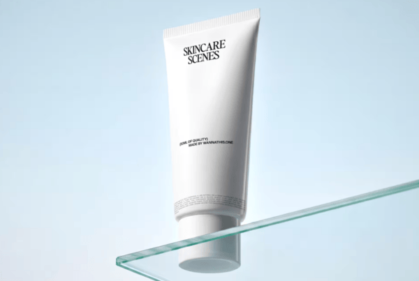 A blank skincare tube standing upright on a transparent glass shelf illuminated by soft, directional studio lighting.