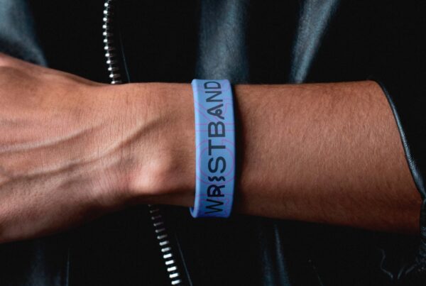 Close-up shot of a person's wrist wearing a customizable light blue rubber wristband, set against a dark leather jacket background.