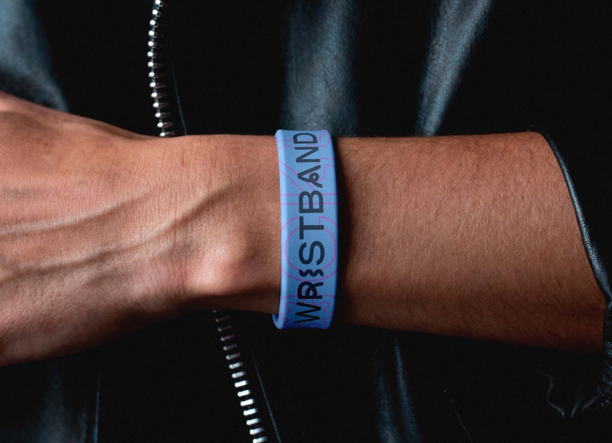 Close-up shot of a person's wrist wearing a customizable light blue rubber wristband, set against a dark leather jacket background.