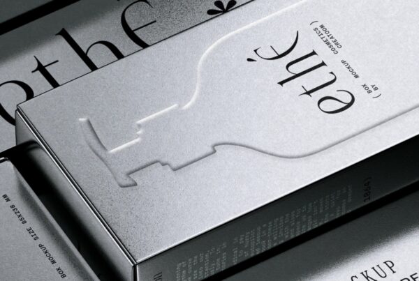 A close-up view of a metallic silver cosmetic box with embossed graphic typography and fine paper texture.